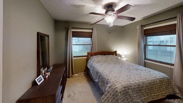 bedroom with ceiling fan, light colored carpet, and a textured ceiling