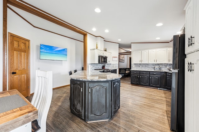 kitchen featuring backsplash, white cabinets, black appliances, light stone countertops, and wood-type flooring