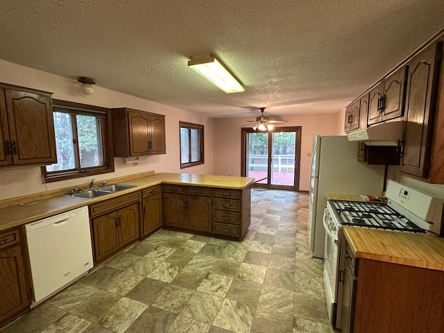 kitchen featuring a textured ceiling, kitchen peninsula, sink, and white appliances