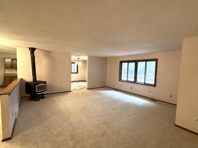 spare room with ceiling fan, a wood stove, a textured ceiling, and light carpet