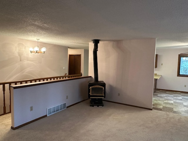 unfurnished living room featuring a textured ceiling, an inviting chandelier, a wood stove, and light colored carpet