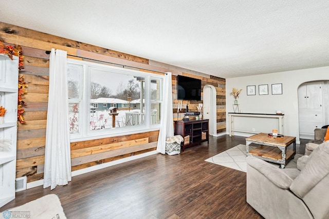 living room featuring a textured ceiling, dark hardwood / wood-style flooring, and wooden walls