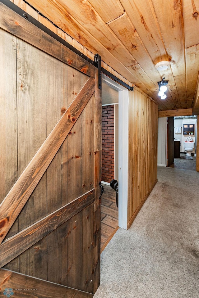 hallway with carpet flooring, a barn door, wooden ceiling, and wooden walls