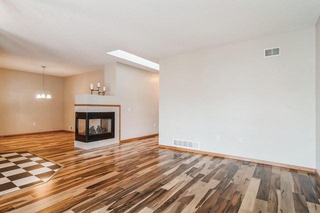 unfurnished living room featuring hardwood / wood-style flooring, a multi sided fireplace, and a chandelier