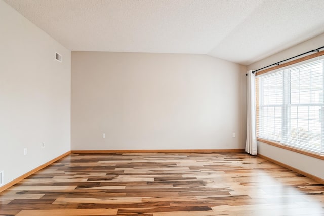 unfurnished room with vaulted ceiling, light hardwood / wood-style flooring, and a textured ceiling