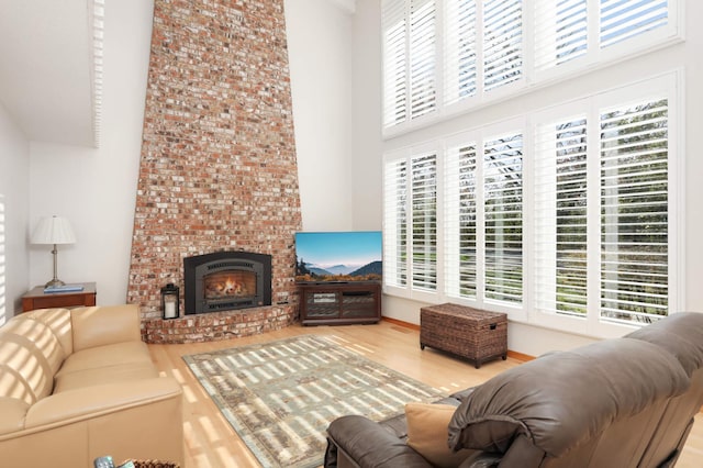 living room with hardwood / wood-style flooring, a towering ceiling, and a brick fireplace