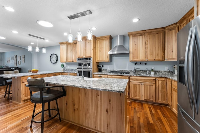 kitchen featuring a kitchen island with sink, a kitchen breakfast bar, wall chimney exhaust hood, and appliances with stainless steel finishes