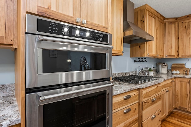 kitchen featuring wall chimney exhaust hood, light hardwood / wood-style flooring, a textured ceiling, stainless steel appliances, and light stone countertops