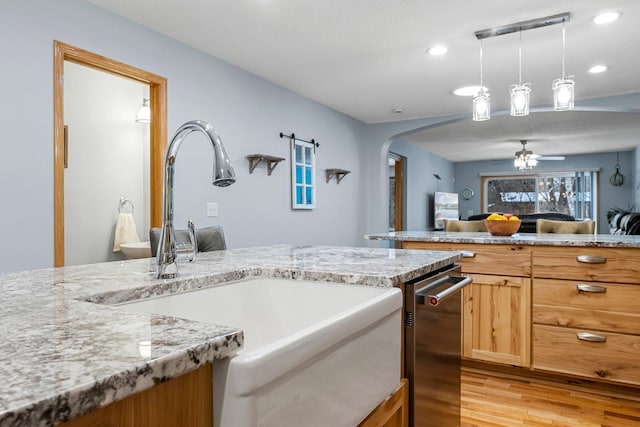 kitchen featuring sink, ceiling fan, hanging light fixtures, light stone counters, and light hardwood / wood-style floors