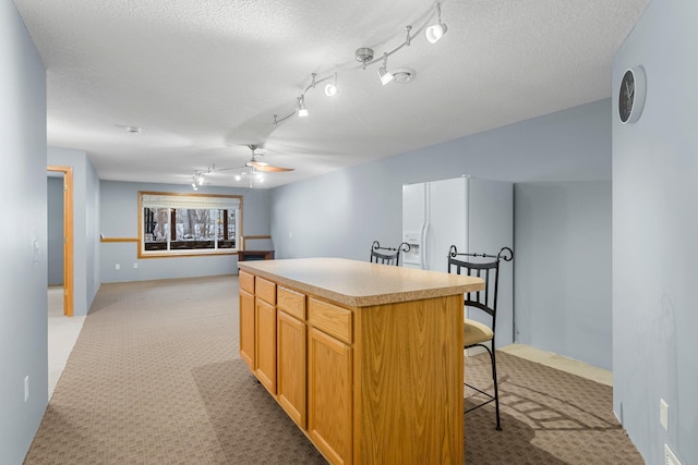 kitchen with ceiling fan, a center island, light carpet, and a textured ceiling