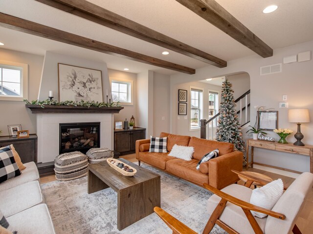 living room featuring beam ceiling, a large fireplace, and light wood-type flooring