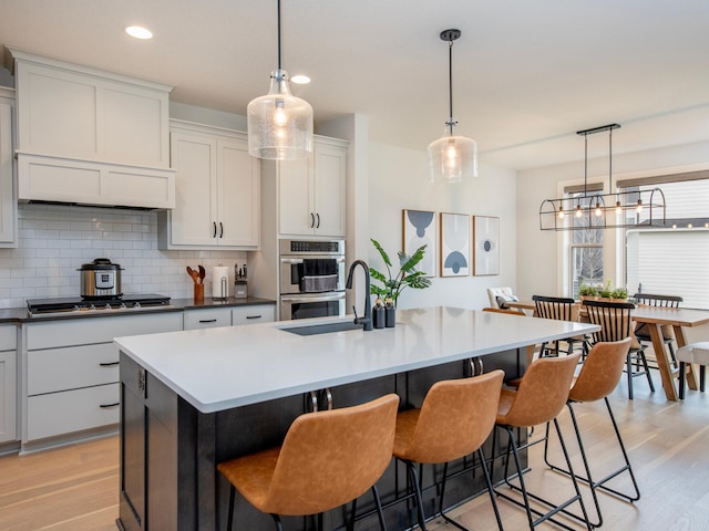 kitchen featuring hanging light fixtures, light wood-type flooring, a kitchen island with sink, and appliances with stainless steel finishes