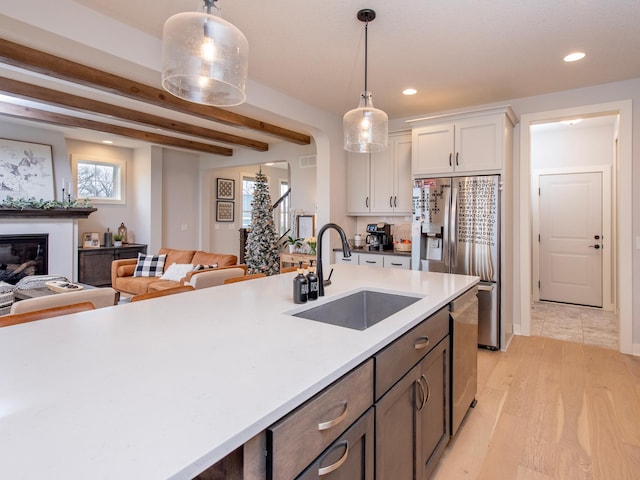 kitchen featuring white cabinetry, sink, hanging light fixtures, stainless steel appliances, and light wood-type flooring