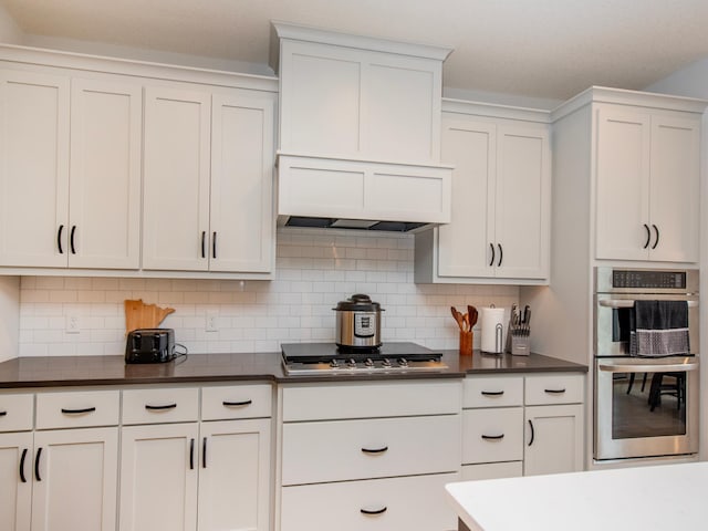 kitchen featuring decorative backsplash, appliances with stainless steel finishes, premium range hood, and white cabinetry