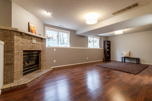 unfurnished living room featuring dark hardwood / wood-style floors, a textured ceiling, and a brick fireplace