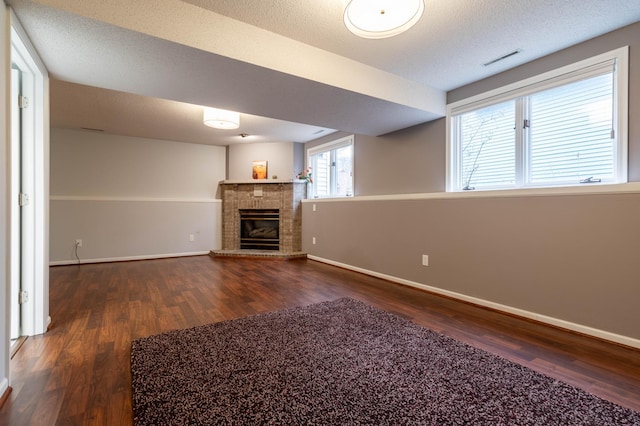 unfurnished living room with a textured ceiling, dark wood-type flooring, and a brick fireplace