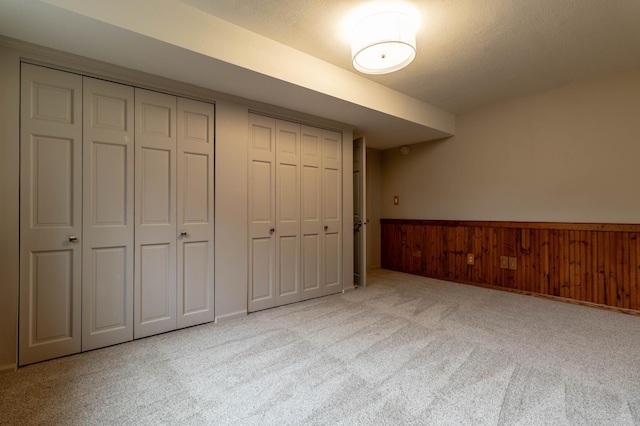 unfurnished bedroom with light carpet, two closets, and wooden walls