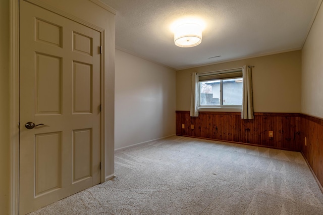 unfurnished room featuring a textured ceiling, light colored carpet, crown molding, and wooden walls