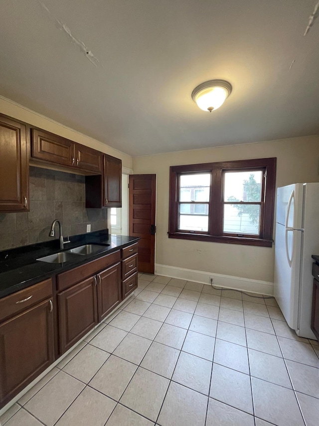 kitchen with sink, decorative backsplash, light tile patterned floors, dark brown cabinets, and white fridge