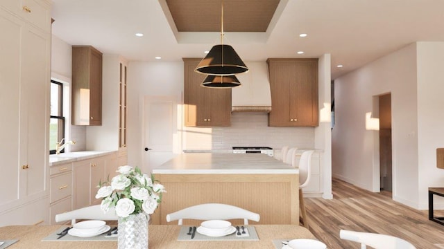 kitchen featuring sink, a raised ceiling, light hardwood / wood-style flooring, pendant lighting, and decorative backsplash