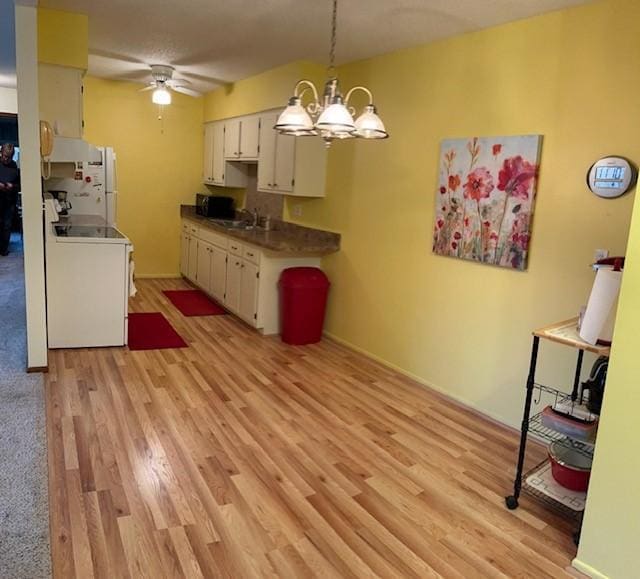 kitchen featuring electric range, pendant lighting, white cabinets, ceiling fan with notable chandelier, and light wood-type flooring