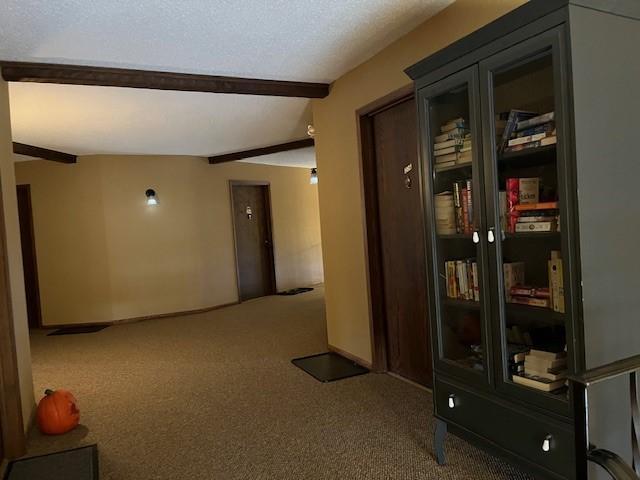 hallway with beam ceiling, carpet, and a textured ceiling