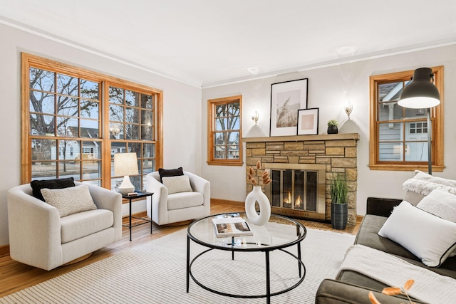 living area with a stone fireplace, crown molding, and wood finished floors