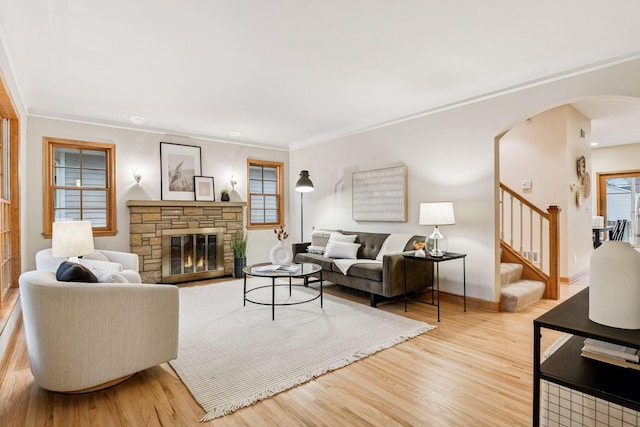 living room featuring ornamental molding, wood finished floors, arched walkways, a stone fireplace, and stairs