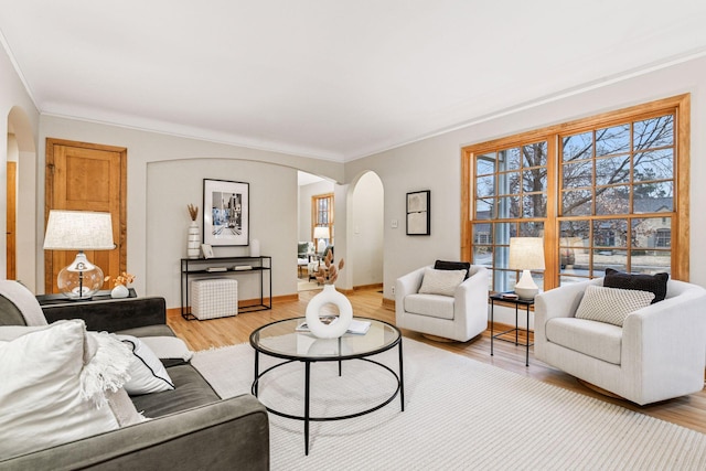 living room featuring ornamental molding, baseboards, arched walkways, and light wood-type flooring