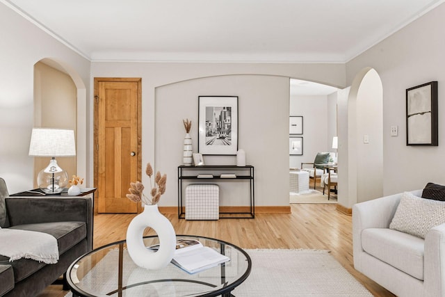 living area with baseboards, arched walkways, wood finished floors, and crown molding