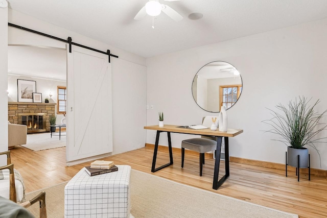 office with light wood-style flooring, a barn door, a fireplace, baseboards, and ceiling fan