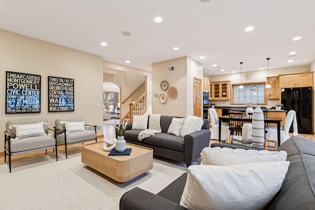 living area featuring arched walkways, stairway, recessed lighting, and light wood-style flooring