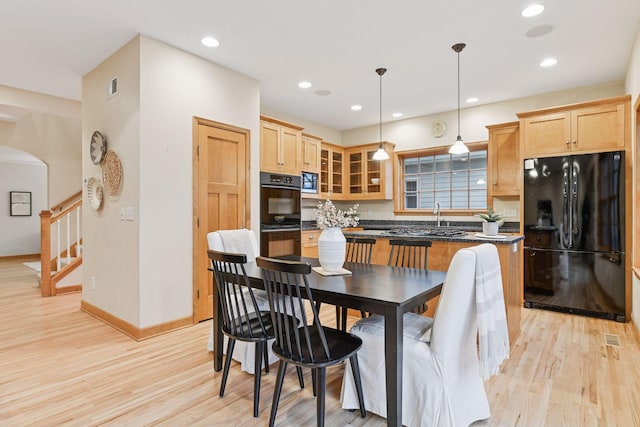 kitchen with light wood-type flooring, dark countertops, black appliances, and light brown cabinets