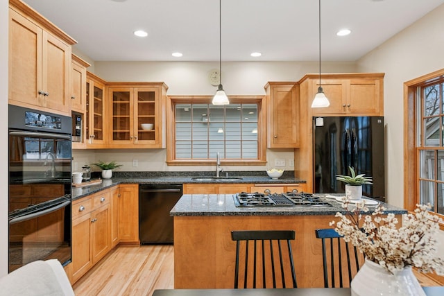 kitchen featuring black appliances, a breakfast bar, light wood-style flooring, a sink, and decorative light fixtures