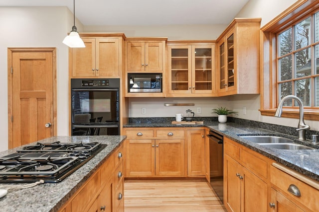 kitchen with glass insert cabinets, dark stone counters, light wood-style floors, black appliances, and a sink