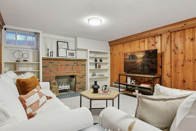 living area with a brick fireplace, built in shelves, wood walls, and a textured ceiling