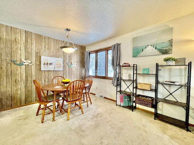 carpeted dining space with wooden walls and a textured ceiling