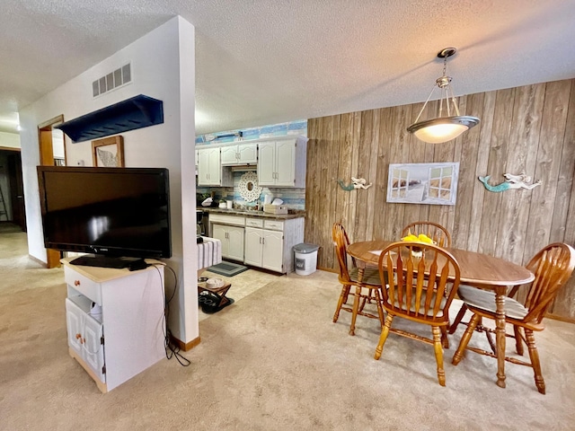 carpeted dining area with a textured ceiling and wooden walls