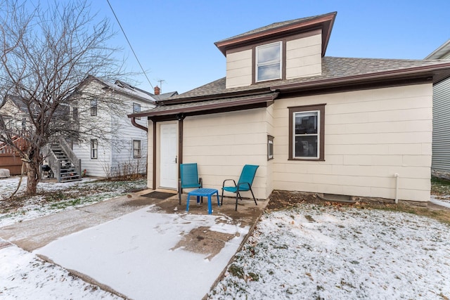 snow covered back of property featuring a patio