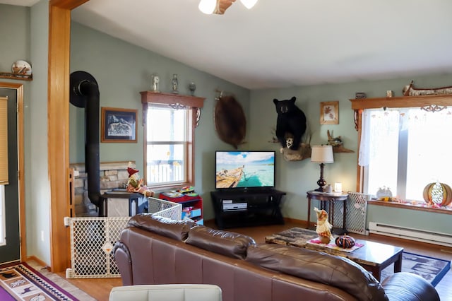 living room featuring lofted ceiling, a wood stove, and a baseboard heating unit