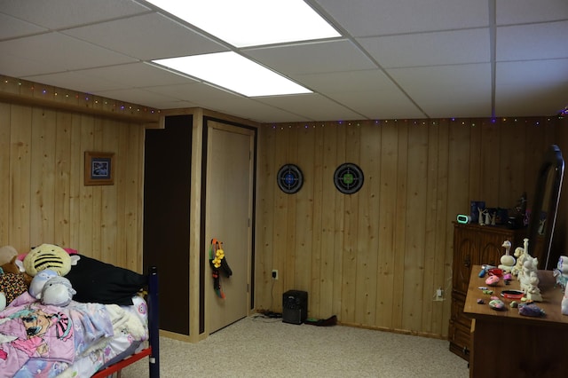 carpeted bedroom featuring wood walls and a drop ceiling