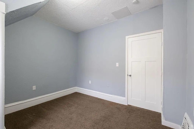 unfurnished room featuring dark carpet, a textured ceiling, and vaulted ceiling