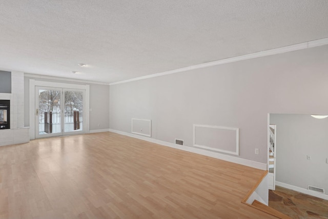 unfurnished living room featuring a tile fireplace, a textured ceiling, light hardwood / wood-style floors, and ornamental molding