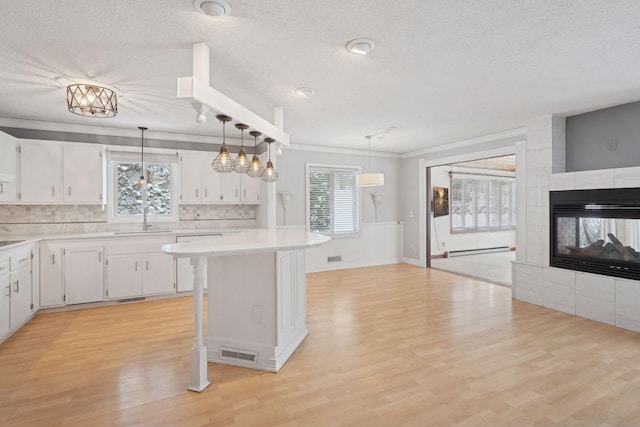 kitchen featuring a tile fireplace, a kitchen breakfast bar, a baseboard heating unit, decorative backsplash, and white cabinets