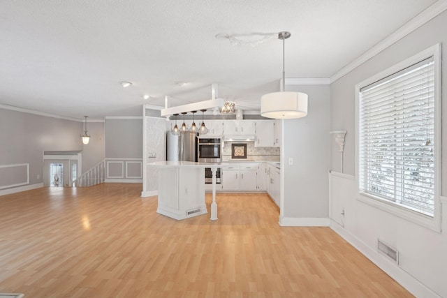 kitchen with appliances with stainless steel finishes, a breakfast bar, crown molding, white cabinets, and hanging light fixtures