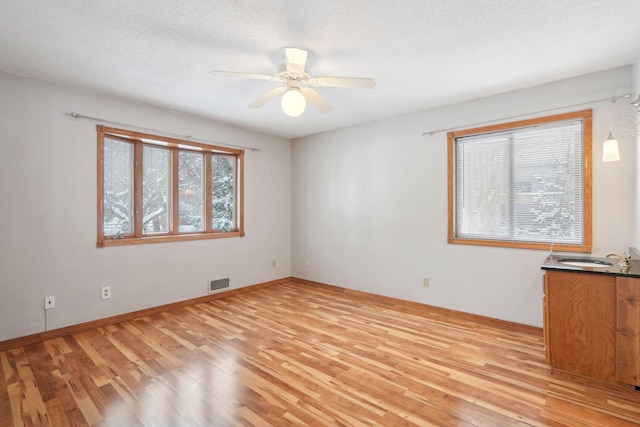 unfurnished room with a textured ceiling, light hardwood / wood-style flooring, ceiling fan, and sink