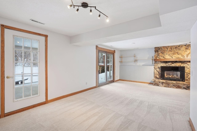 unfurnished living room featuring a stone fireplace, light colored carpet, rail lighting, and a wealth of natural light