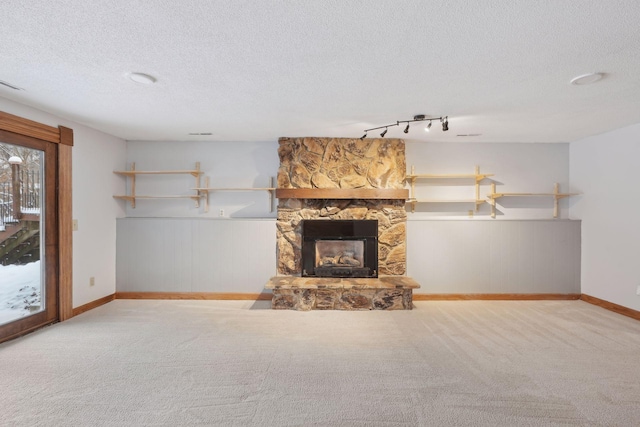 unfurnished living room with a textured ceiling, a fireplace, rail lighting, and light carpet