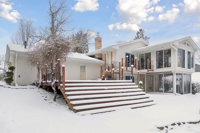 snow covered back of property with a sunroom