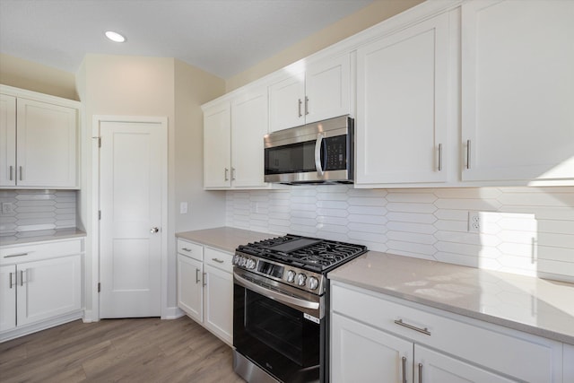 kitchen with decorative backsplash, light stone countertops, light hardwood / wood-style floors, white cabinetry, and stainless steel appliances